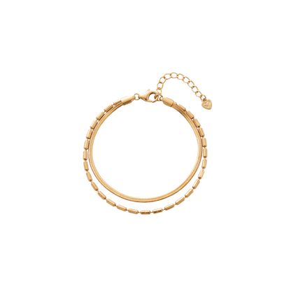 A gold-toned double-strand chain bracelet with a textured outer chain, a smoother inner chain, a lobster clasp, and an extender chain with a small heart-shaped tag, shown on a plain white background.