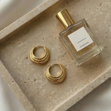 chunky layered gold hoop earrings next to perfume aesthetic luxury flat lay