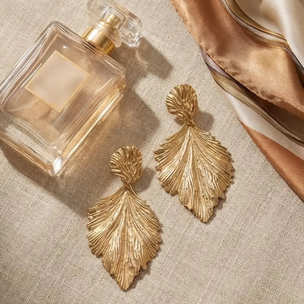 Gold leaf earrings next to a perfume bottle on a textured surface