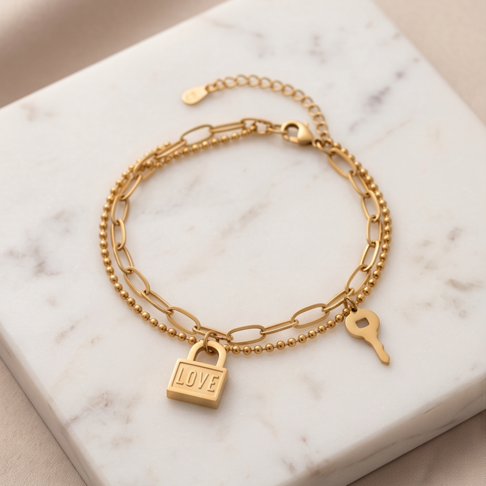 Gold bracelet with padlock and key charms on a marble surface
