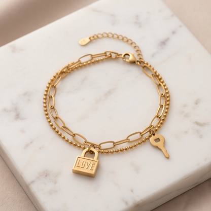 Gold bracelet with padlock and key charms on a marble surface