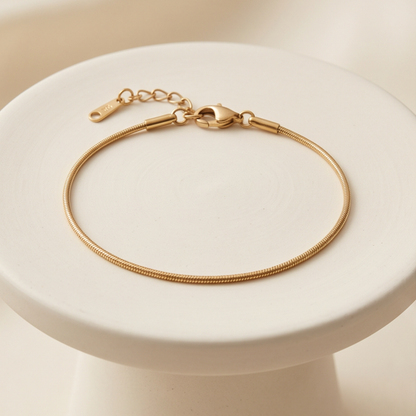 Gold bracelet on a white pedestal with a beige background