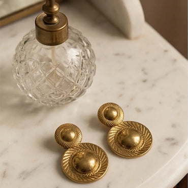 gold vintage statement earrings flat lay with perfume textured luxury jewelry