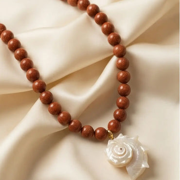 Goldstone beaded necklace with mother of pearl shell pendant flat lay handmade jewelry Julie Saldivia