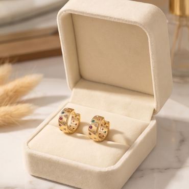 Gold hoop earrings with gemstones in a beige jewelry box on a marble surface.