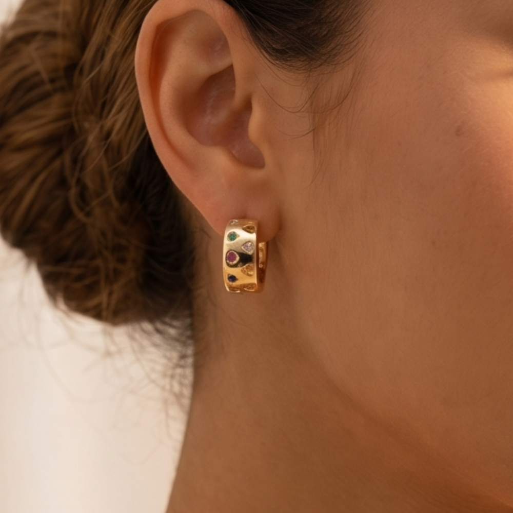 Gold hoop earring with embedded gemstones worn by a person.