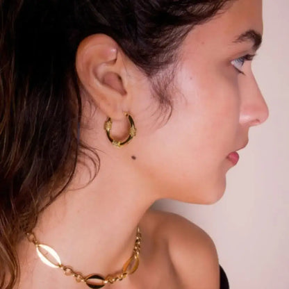 Close-up of a person wearing gold hoop earrings and a necklace against a neutral background