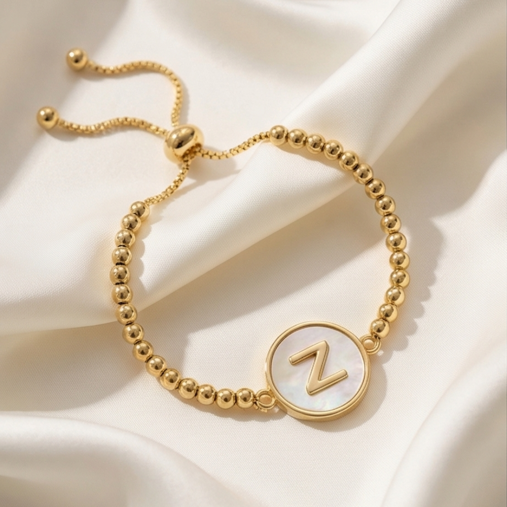 Gold bracelet with a circular charm featuring the letter 'Z' on a beige fabric background