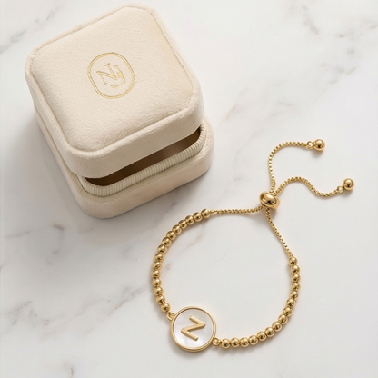 Gold bracelet with a letter 'Z' charm on a marble surface next to a jewelry box.