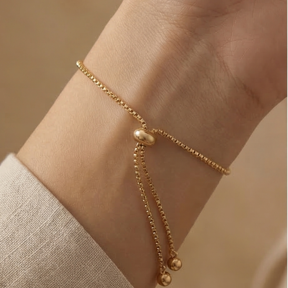 Gold bracelet adjustable on a wrist with a plain background