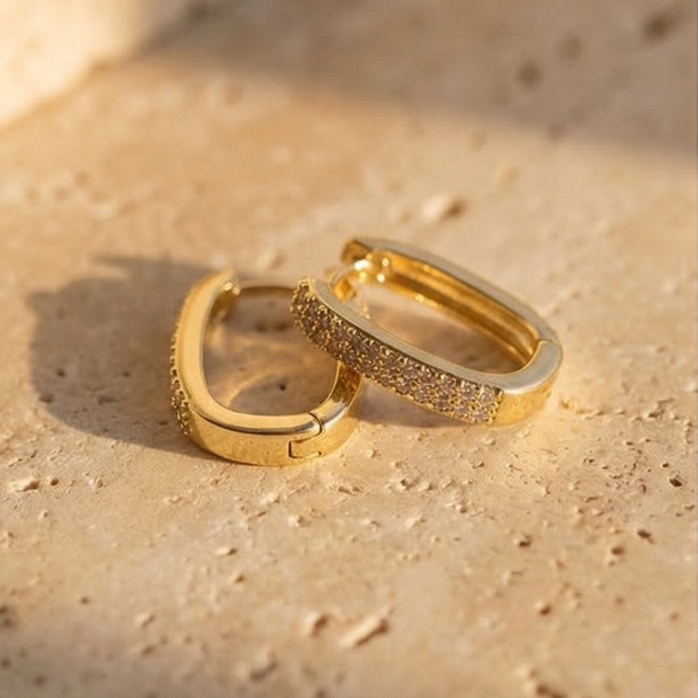 Two gold hoop earrings on a sandy surface