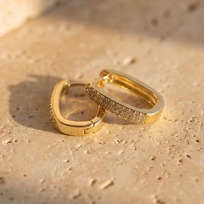 Two gold hoop earrings on a sandy surface