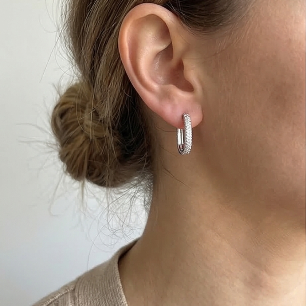 Close-up of an ear wearing a diamond hoop earring with a neutral background