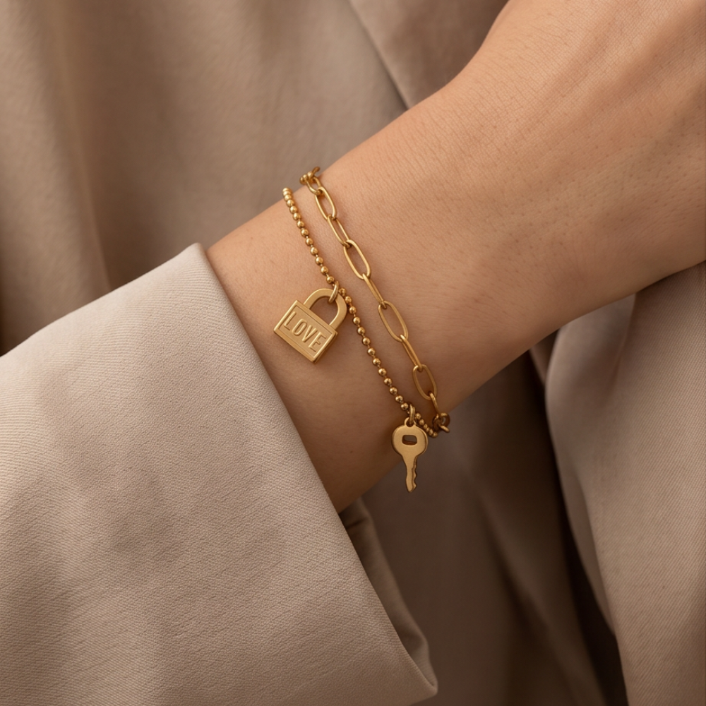 Gold bracelet with lock and key charms on a wrist against a beige background