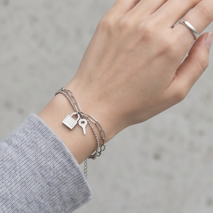 Hand wearing a silver bracelet with padlock and key charms on a blurred background