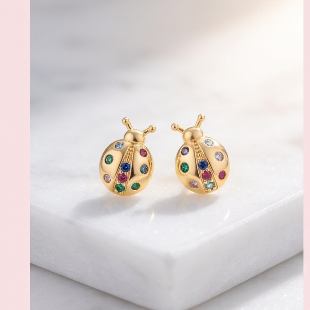 Pair of 18K gold plated ladybug earrings displayed on white marble