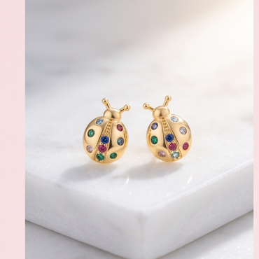 Pair of 18K gold plated ladybug earrings displayed on white marble