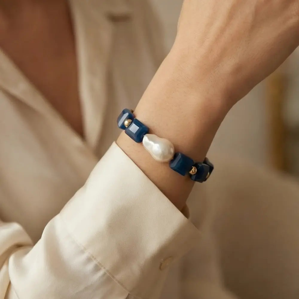 Navy blue bracelet with a pearl and gold accents on a wrist, against a neutral background.