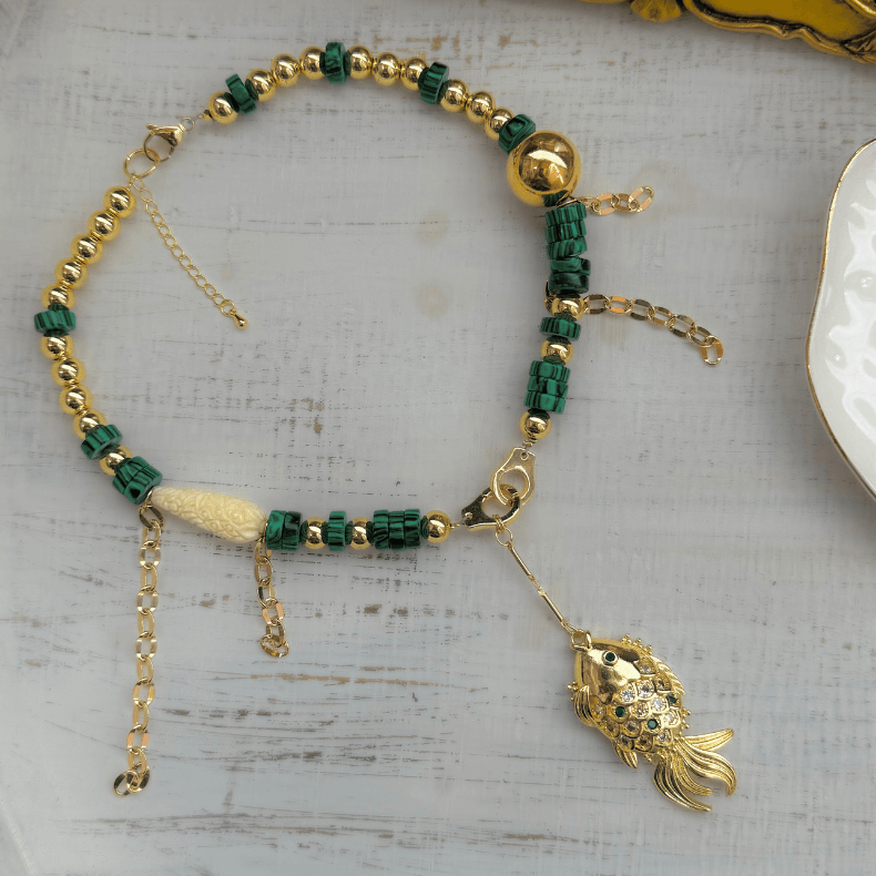 16-inch 18k gold-plated necklace featuring malachite stones and a unique fish charm with an emerald green rhinestone, designed to add a touch of sophistication and coastal charm to any outfit."