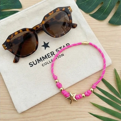Sunglasses and pink bracelet with star accents on a 'Summer Star Collection' branded cloth, surrounded by green leaves.