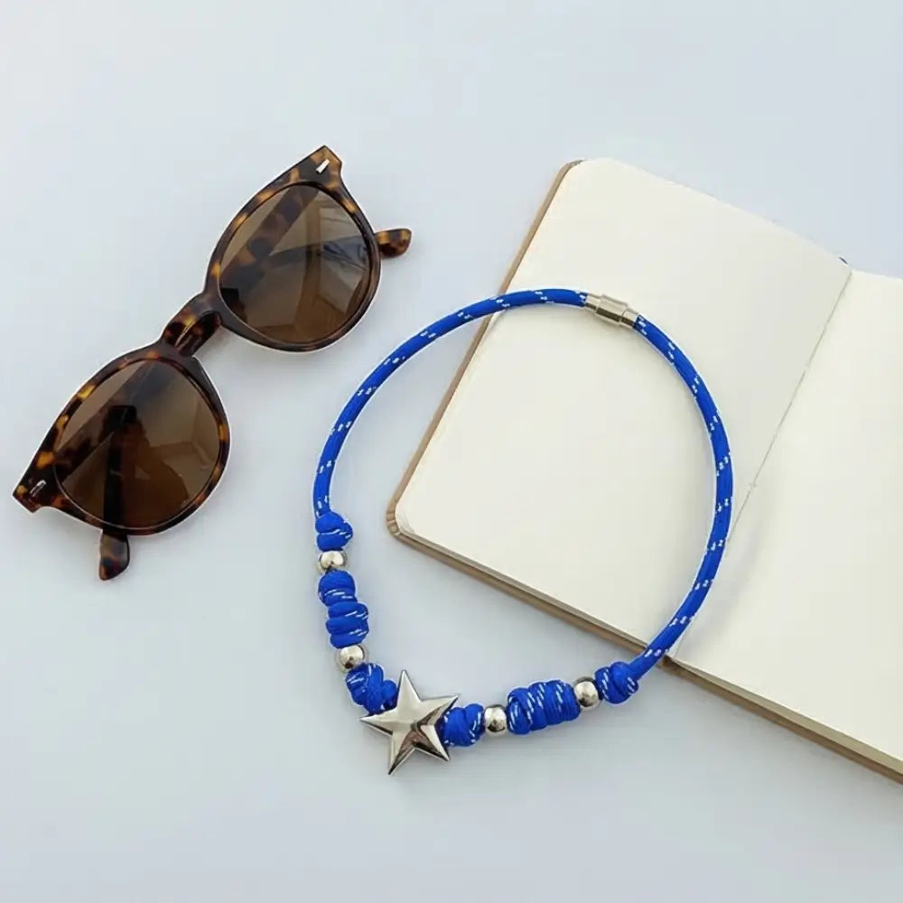 Blue beaded necklace with a star pendant on a light gray surface with sunglasses and an open book.