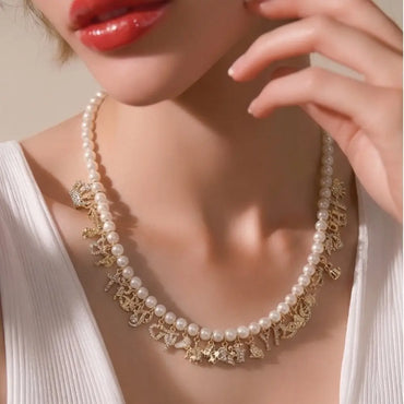 Pearl necklace with gold charms worn by a person against a neutral background