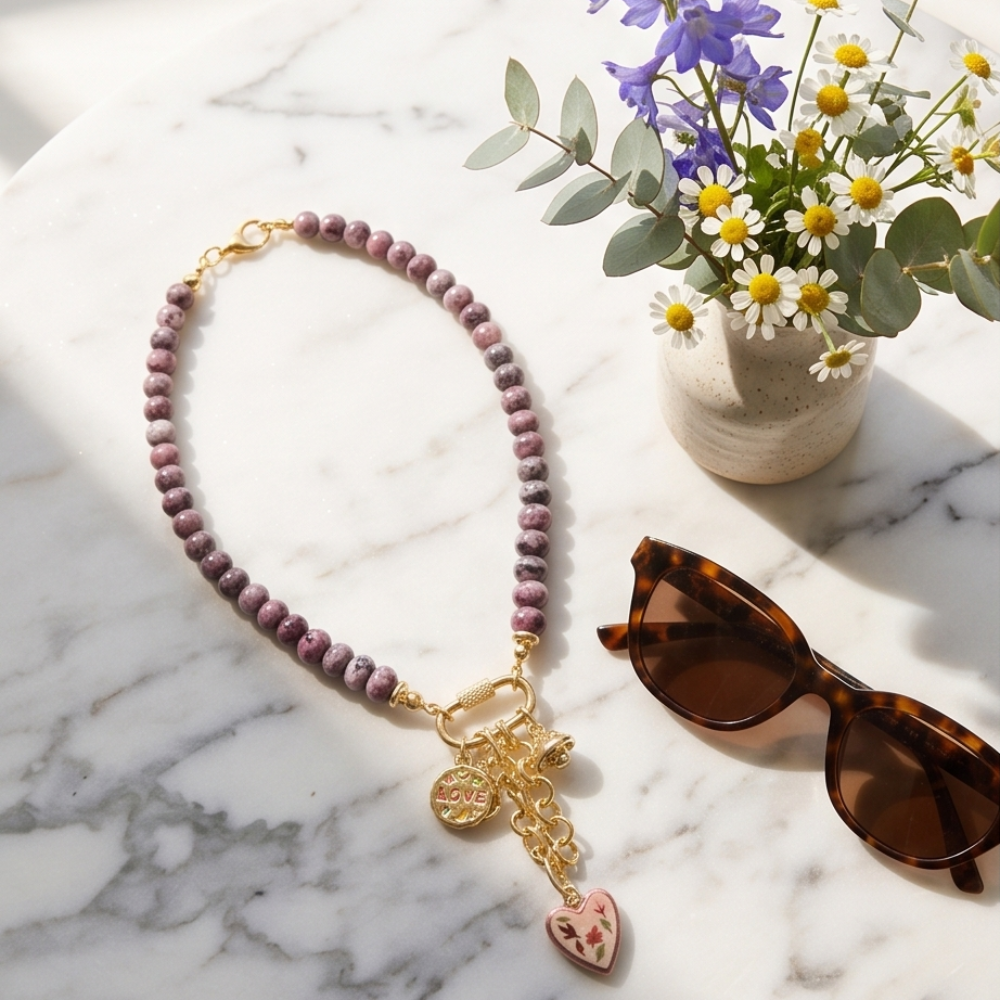 Necklace with a cross pendant on a marble surface with sunglasses and flowers.