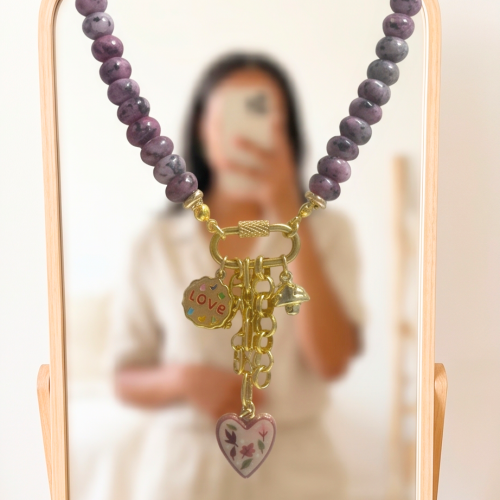 Necklace with purple beads and gold charms on a stand with a blurred background