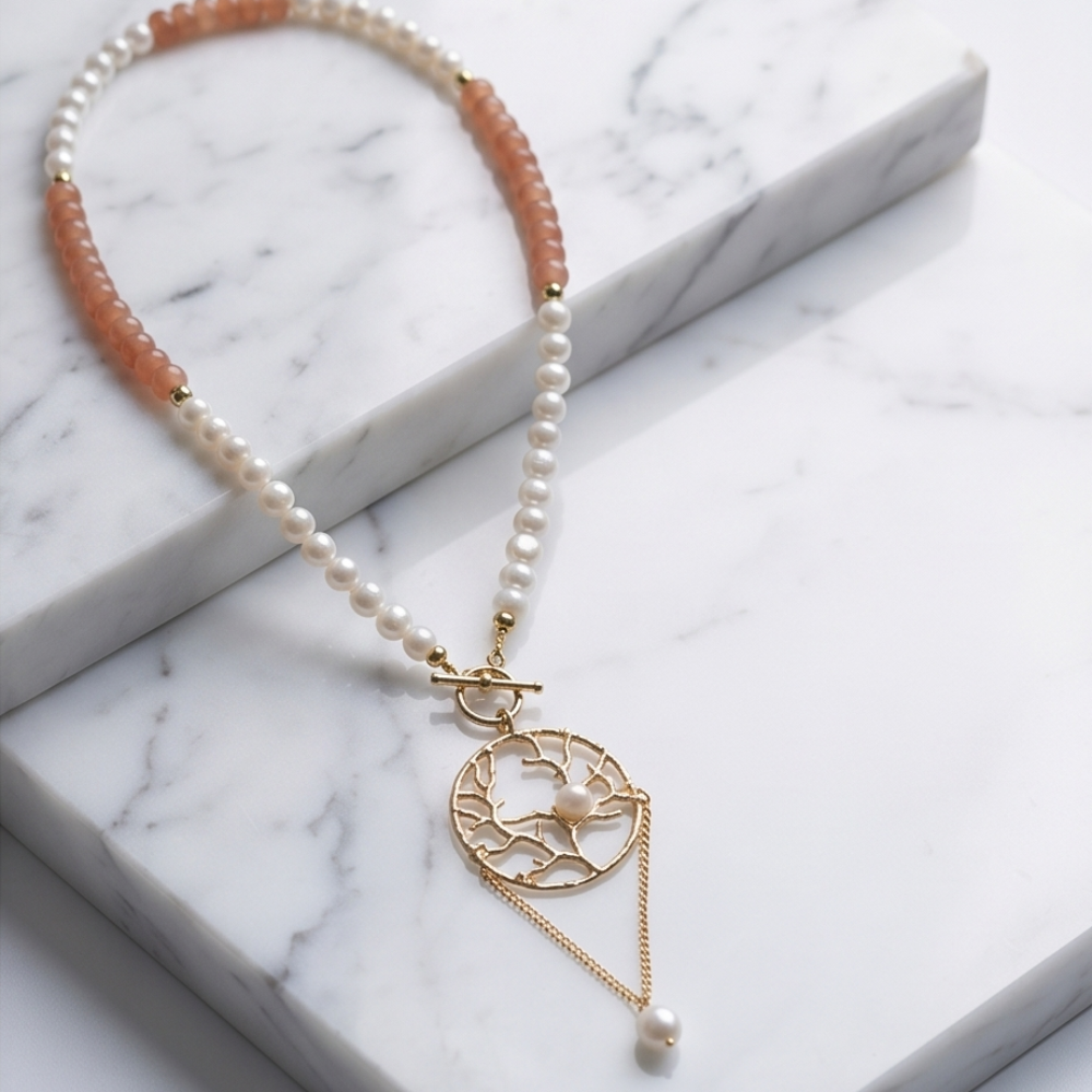 Pearl and blush beaded Tree of Life necklace displayed on white marble slab