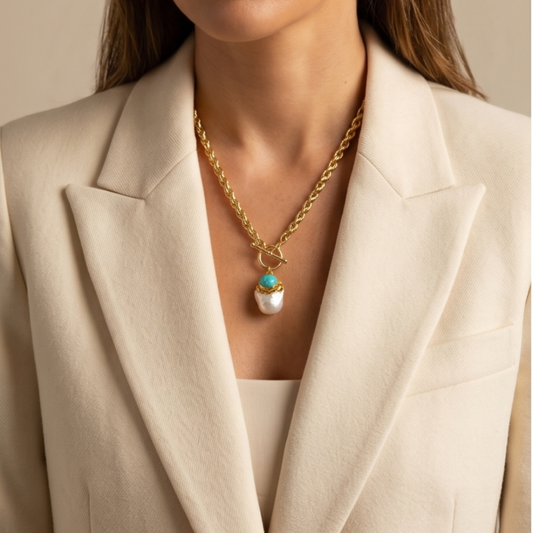 Gold necklace with a pendant worn by a person in a beige blazer.