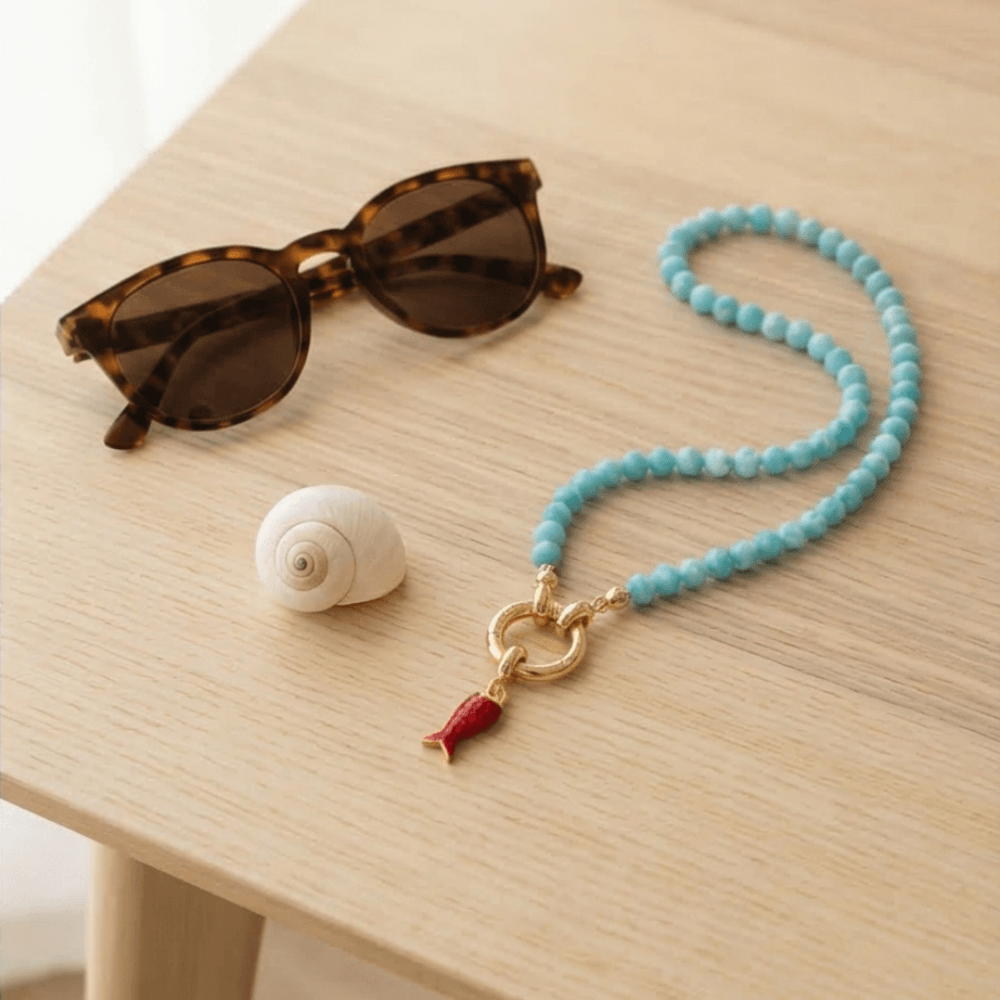 turquoise beaded necklace with gold clasp and red charm on table lifestyle jewelry Julie Saldivia