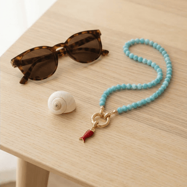 turquoise beaded necklace with gold clasp and red charm on table lifestyle jewelry Julie Saldivia
