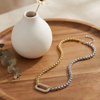 Two-tone gold and silver chain necklace styled on wooden tray with minimalist decor modern luxury jewelry
