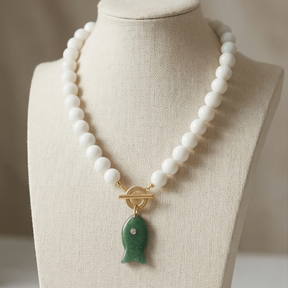 White beaded necklace with green fish pendant on display bust modern elegant jewelry