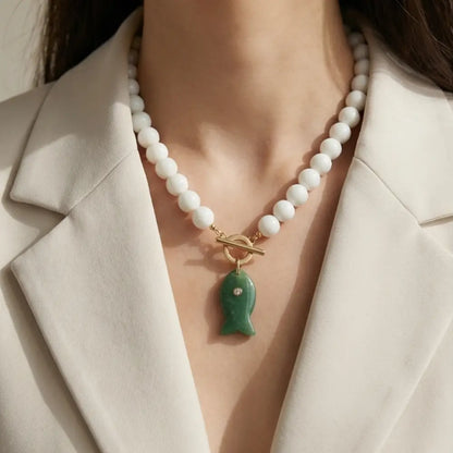 Woman wearing white beaded necklace with green fish pendant elegant statement jewelry